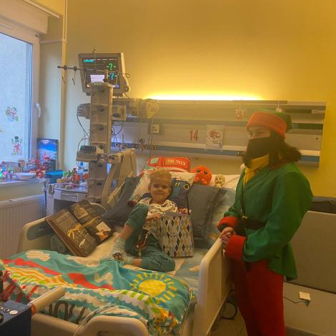 uśmiechniete dziecko z prezentami otoczone aparaturą medyczną, Elf stoi przy łóżku