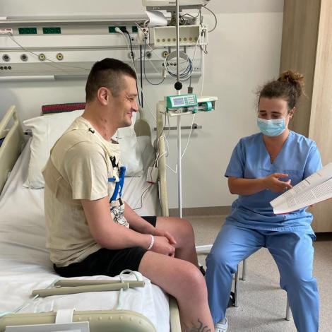 Rehabilitantka z broszurą w rękach instruuje chorego siedzącego na łóżku