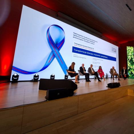 Sześcioro panelistów podczas debaty o transplantacjach dziecięcych. W tle symboliczna wstążka 
