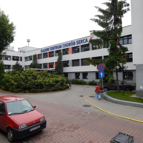 główne wejście do budynku A Śląskiego Centrum Chorób Serca otoczone klombami zieleni, widać również dwa samochody i przechodzących ludzi