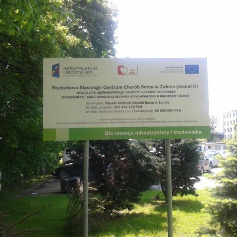Tablica informacyjna dotycząca rozbudowy SCCS postawiona wśród zieleni