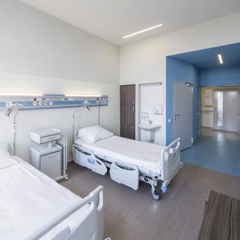 sala dla pacjentów, łóżka z szafkami,  w niebieskim wejściu drzwi do łazienki