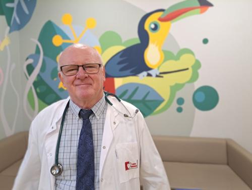 Prof. Białkowski ze stetoskopem na szyi. W tle rysunek kolorowego tukana. 