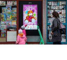 Dwójka dzieci z mamą stojące przy wystawie z plakatem misia