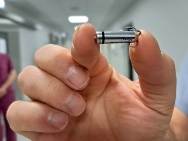 Zbliżenie na urządzenie wielkości kapsułki z lekiem, trzymane między palcami lekarza. 